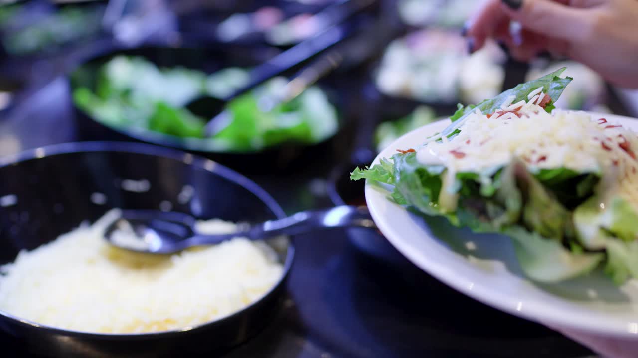 Primo piano di una donna che versa formaggio grattugiato su un'insalata verde a un buffet self-service