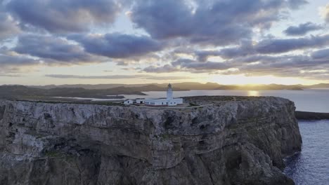 Toma-Aérea-De-Establecimiento-En-El-Faro-De-Cavalleria-Menorca-Acantilado-Marino-Fondo-Del-Horizonte-Del-Atardecer,-Viaje-Destino-Natural-Español