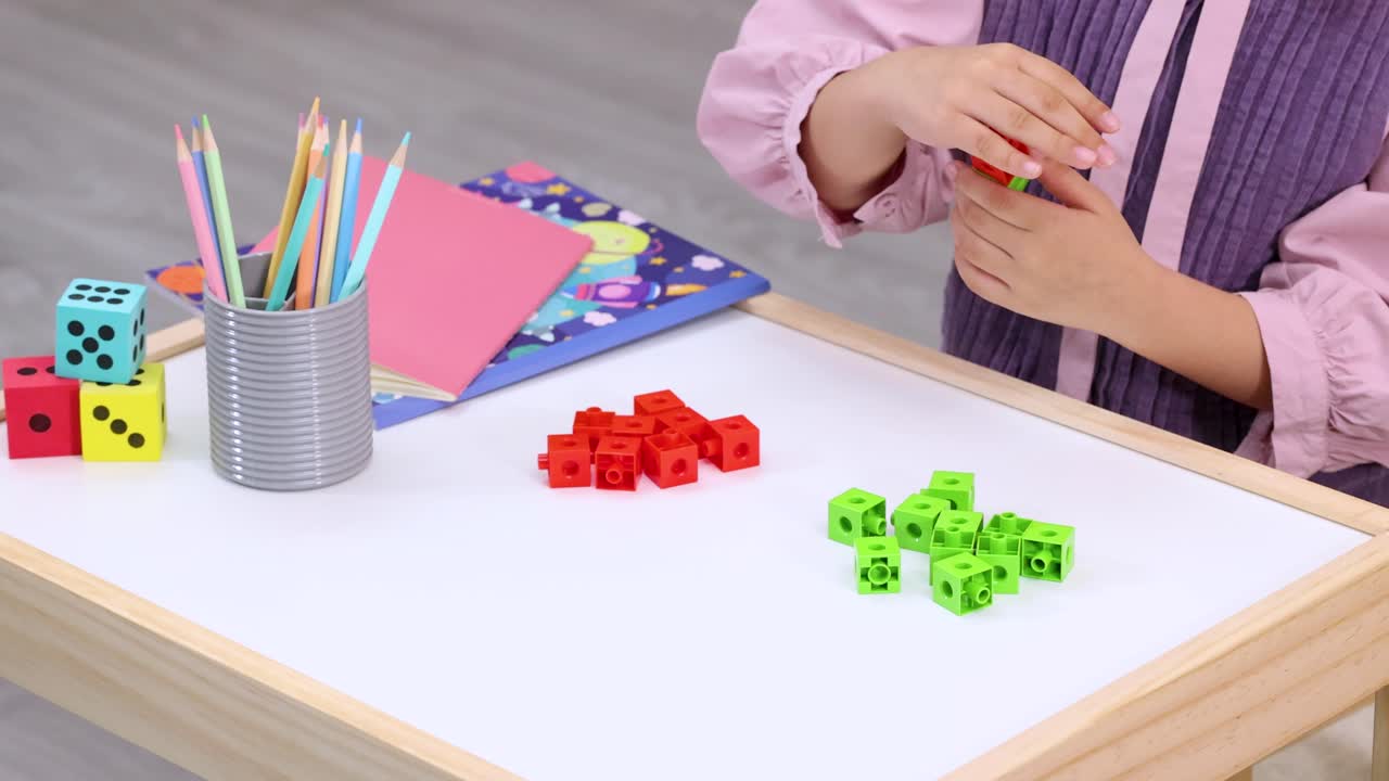 Child assembles interlocking counting cubes on bright classroom table with school supplies and overhead view