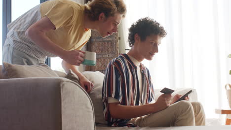 una pareja gay feliz y diversa usando un teléfono inteligente para comprar en línea en el sofá en casa, en cámara lenta