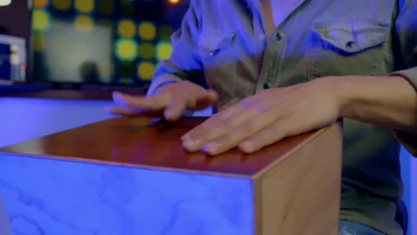 Musician-Playing-Percussion,-Wooden-Bongo,-Colorful-Lights-In-Background