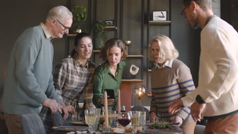 Mujer-Tomando-Una-Foto-De-La-Comida-En-La-Mesa-Y-Mostrándole-Una-Foto-A-Su-Familia-Parada-Junto-A-Ella-En-Casa