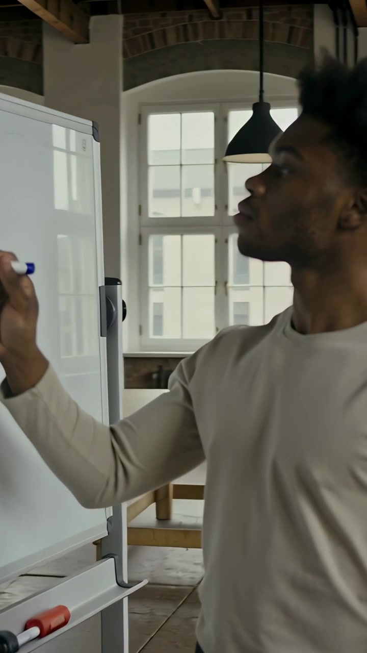 Vertical video: Holding blue marker, beige-shirted man writing on board to plan in loft, copy space