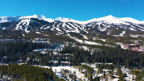 beautiful snow covered winter mountain peaks aerial drone view with ski trails ready for outdoor sports and adventure in thick pine tree forest