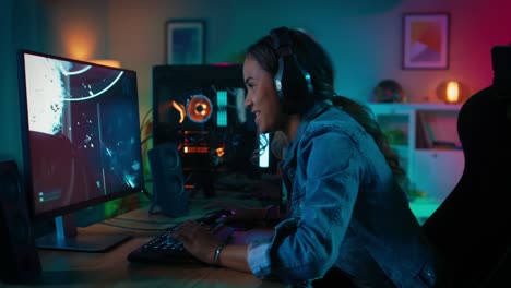 y muy emocionado chica jugador negro en auriculares está jugando y ganando en primera persona shooter videojuego en línea en su computadora. habitación y pc tienen coloridas luces de neón led. noche acogedora en casa.
