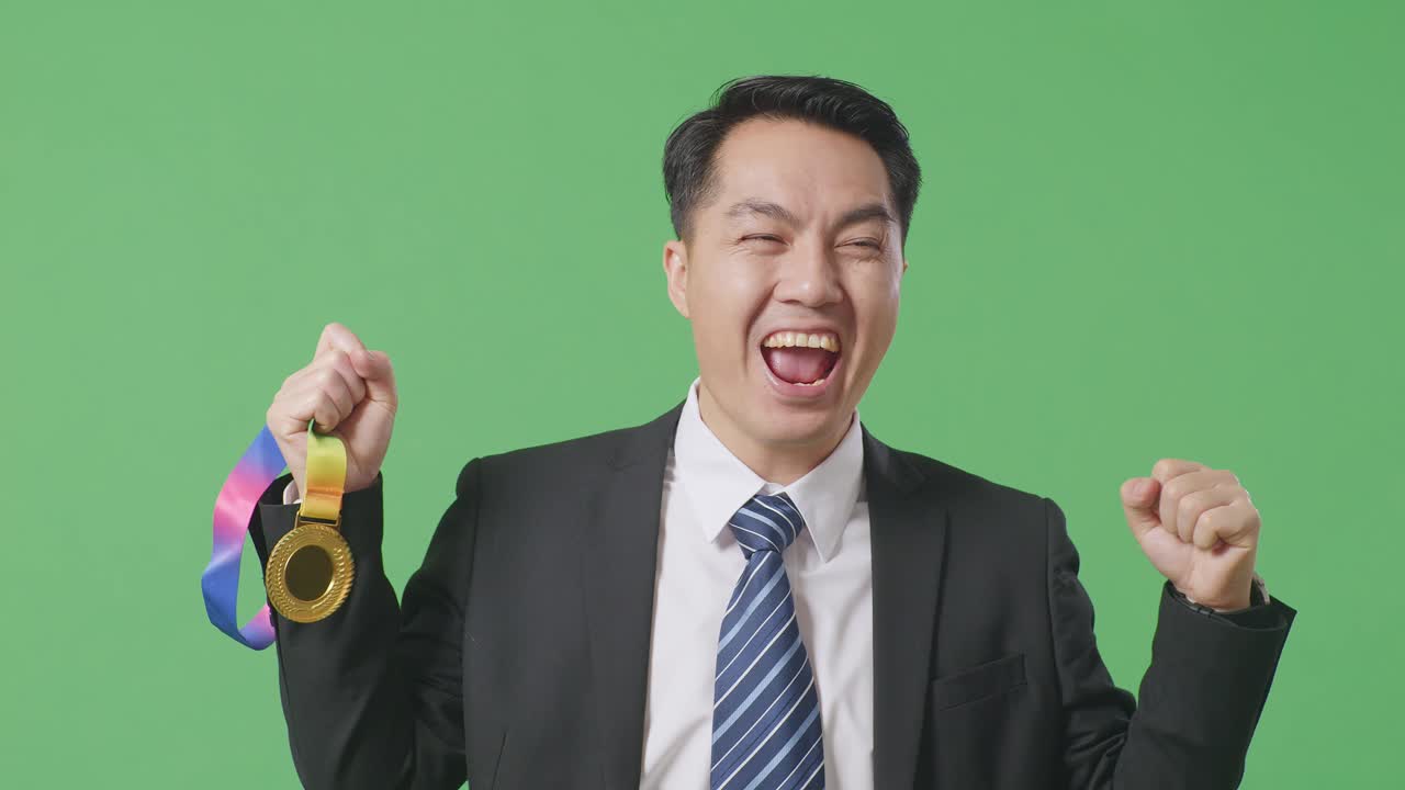 슈트와 타이를 입은 아시아 사업가, 금메달을 바라보며 울부는 골, 첫 우승을 축하하는 장면, 녹색 스크린 배경, 스튜디오