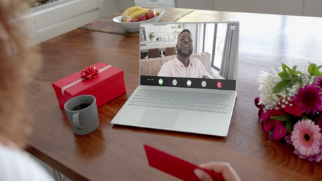 Caucasian-woman-holding-envelope-and-talking-with-african-american-man-on-laptop-screen