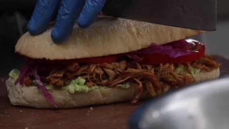 chopped chicken sandwich with purple cabbage, sliced tomatoes, and avocado spread in ciabatta bread, being cut by a chef