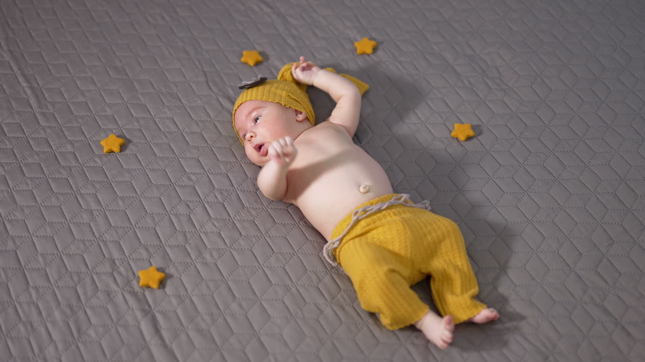 Nice sweet child in yellow funny costume lies on the grey background. Baby moving his lovely little hands actively. Little stars next to the boy.