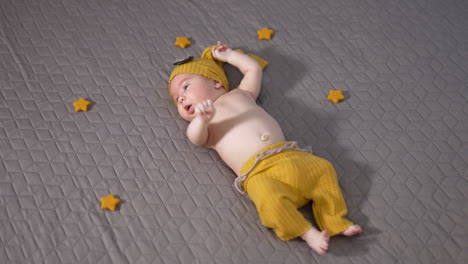 nice sweet child in yellow funny costume lies on the grey background. baby moving his lovely little hands actively. little stars next to the boy.