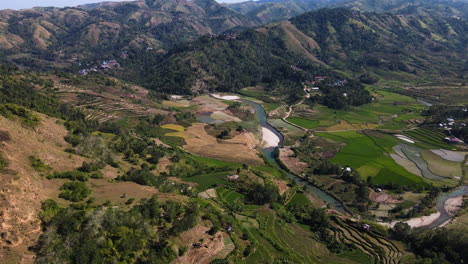 panoramic aerial view of mountains, terrace rice fields, and river near pantai watu bella, sumba island, indonesia