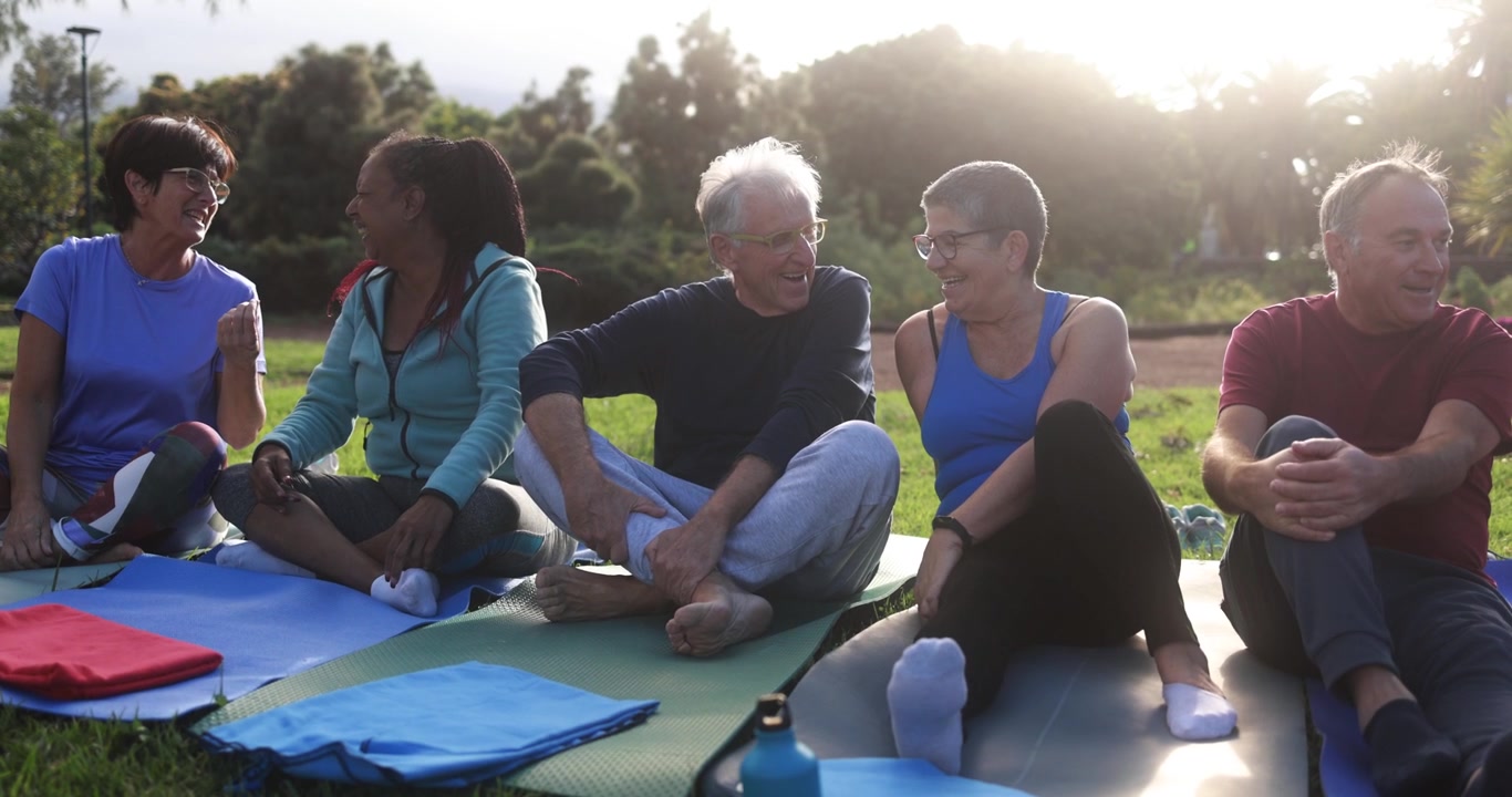 Happy Senior People Talking and Laughing on Yoga Mats in a Park
