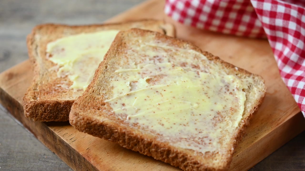 Hand Picking Up a Slice of Buttered Toast from a Wooden Board