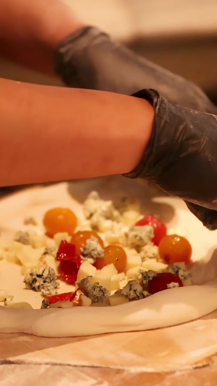 Chef che prepara una pizza gourmet con pomodorini e formaggio erborinato