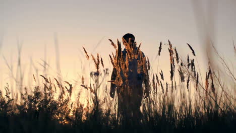 A-Young-Backpacker-Walks-Through-A-Wheat-Field-At-Dusk