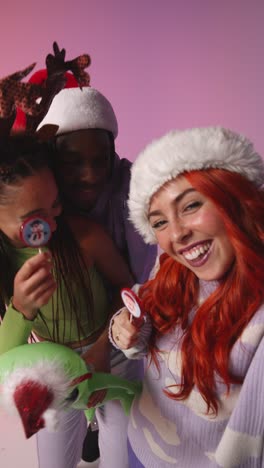 Vertical-Video-Studio-Shot-Of-Gen-Z-Friends-Dancing-And-Posing-For-Selfie-At-Christmas-Party-Wearing-Santa-Hat-And-Reindeer-Antlers-1