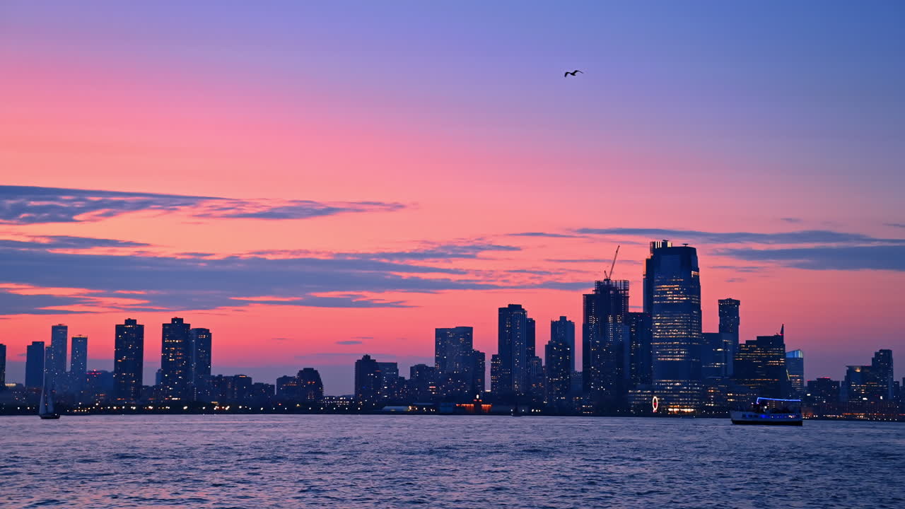 Dark silhouettes of the buildings in the skyline of New York at the backdrop of pink sky. View on the city at dusk time from the river