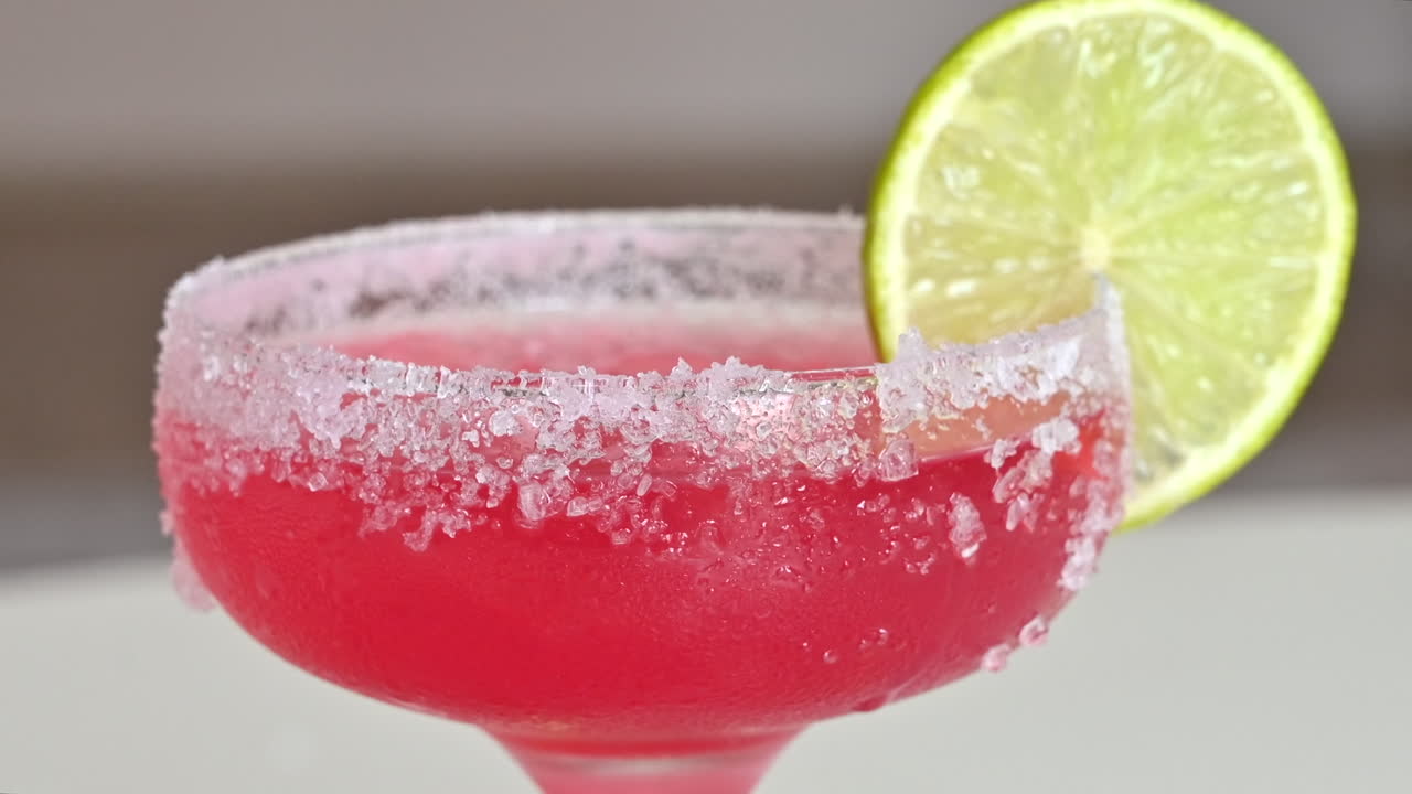 Primer plano de un cóctel rojo claro con hielo y rodajas de lima