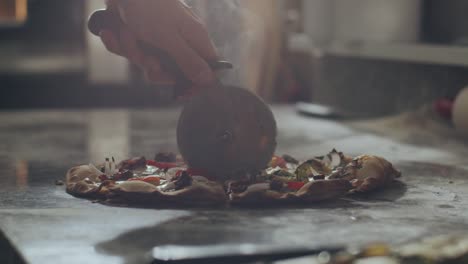 pizzaiolo cutting fresh hot pizza