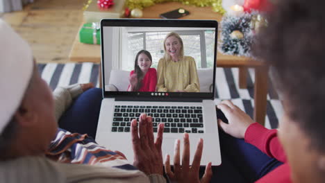 african american mother and daughter using laptop for christmas video call with family on screen