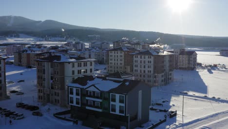 Drone-flying-away-from-hotel-in-snow-covered-landscape-with-sunset-rays-at-ski-resort