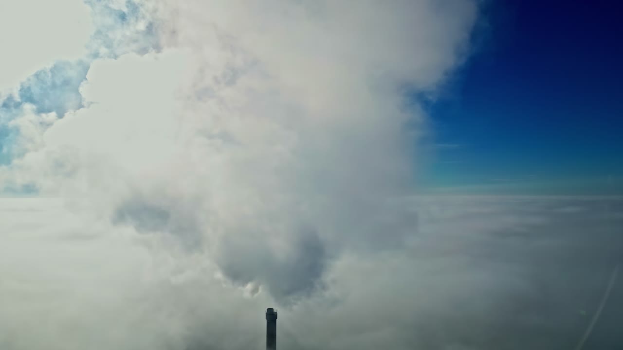 Ein dampfender Schornstein vor grauen Wolken unter blauem Himmel. Luftaufnahme.