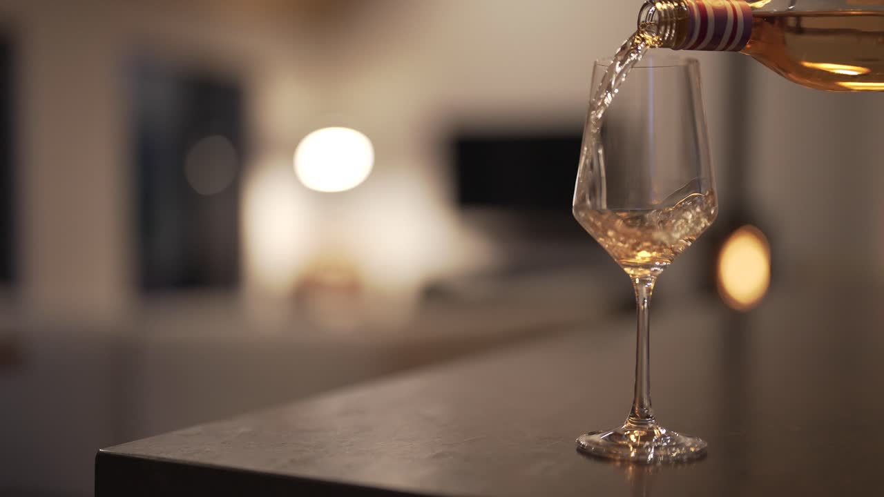 movimento lento di una bottiglia di vino bianco versato in un bicchiere con sfocato fantasia casa moderna soggiorno sullo sfondo