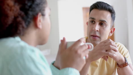 Pareja-Masculina-Gay-Diversa-Enfocada-Sentada-En-La-Mesa,-Tomando-Café-Y-Hablando-En-Casa,-Cámara-Lenta