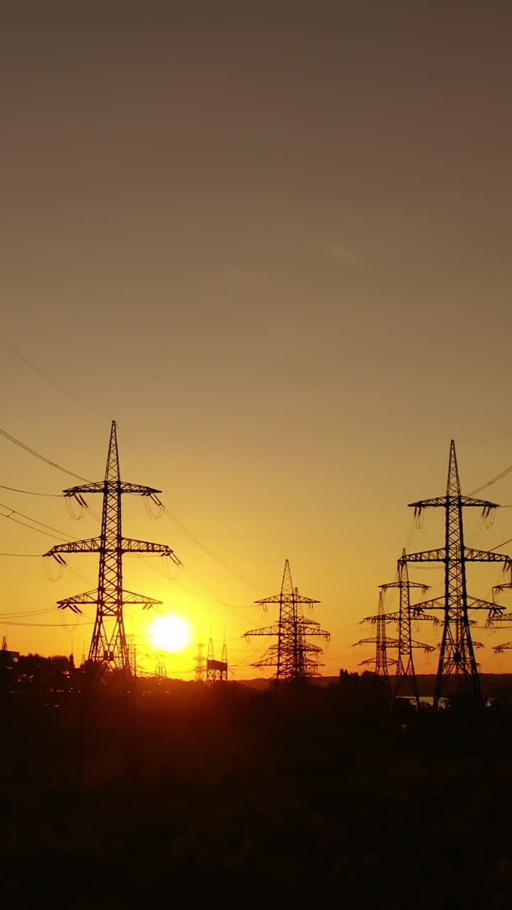 Electric power station in the evening. High voltage electric lines against the setting sun. Transmission lines. Motion camera back. Vertical video