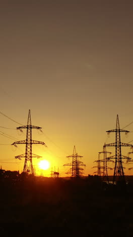 electric power station in the evening. high voltage electric lines against the setting sun. transmission lines. motion camera back. vertical video