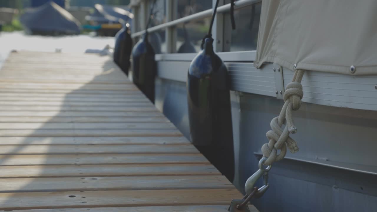 Black Buoy Attached On The Hull And Railings Of A White Boat With A Knotted Rope Attached On A Metal Hook And Moored At The Wooden Pier. - close up shot