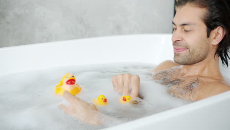 man relaxing in a bathtub with rubber ducks