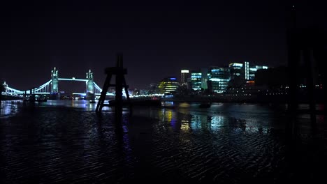 london skyline at night, view of tower bridge, buildings and skyscrapers from the river thames at low tide, beautiful light reflections in the water