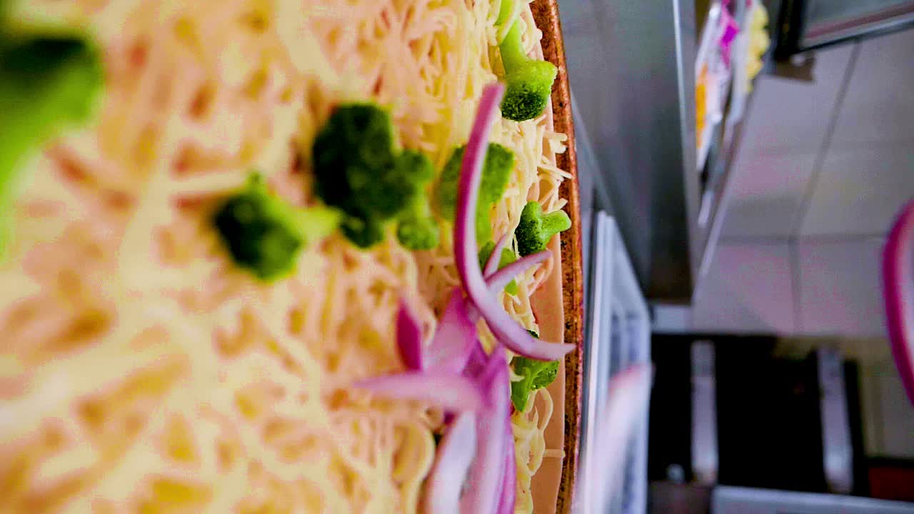 movimiento lento vertical dolly tiro moviéndose hacia atrás de una pizza con brócoli, queso y salsa de tomate como cebollas caen sobre él, la pizza está encima