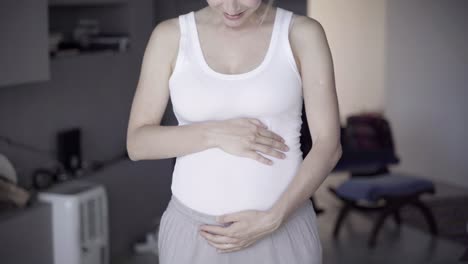 Smiling-pregnant-lady-standing-and-rubbing-belly