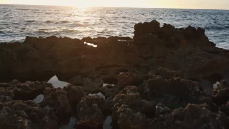 Tiefflug-über-Felsenbecken-Und-Hinaus-Aufs-Meer-Mit-Kabbeligen-Wellen-Während-Des-Sonnenuntergangs-In-Cala-Xarraca