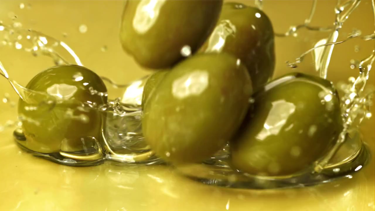 Primo piano di olive che cadono e schizzano nell'olio d'oliva.
