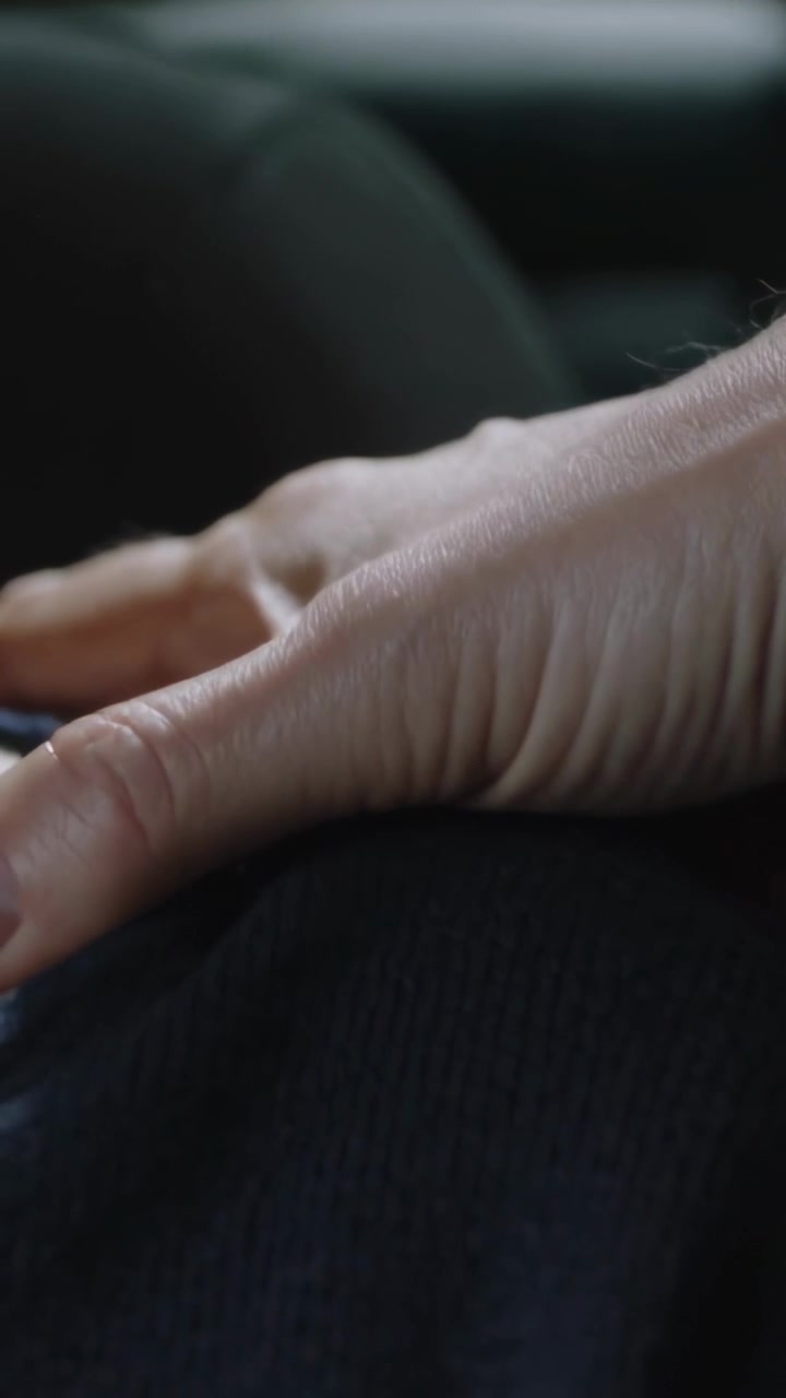 Vertical video: Placing right hand on dark pants knee, making slow shifts inside car near headrest
