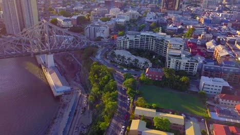 Tilting-up-aerial-view-of-a-city-street-and-a-bridge-over-a-river-at-sunset