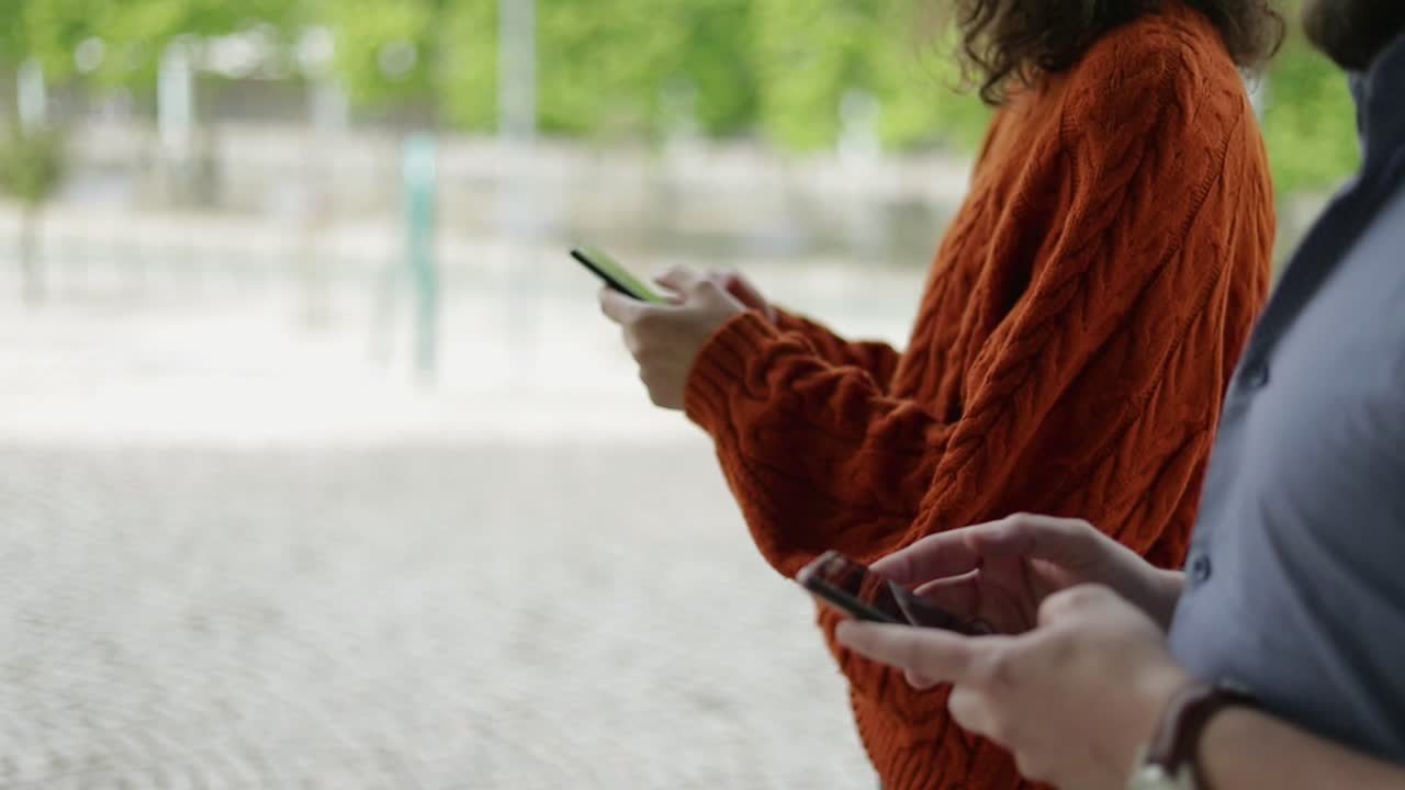 Inquadratura ravvicinata di coppia che usa gli smartphone all'aperto.