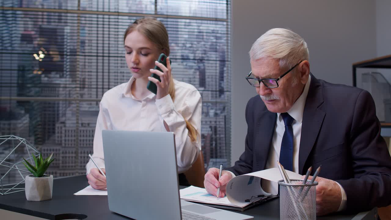 mujer secretaria hablando por teléfono móvil, hombre de negocios sénior jefe trabajando en la computadora portátil en la oficina
