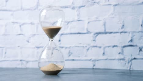 hourglass on a table against a white brick wall