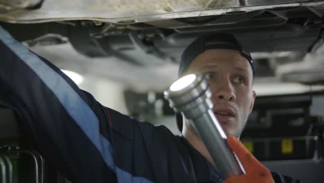 mechanic in uniform repairing a car underside using tools.