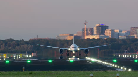 avión aterrizando en la pista al atardecer con la ciudad en el fondo