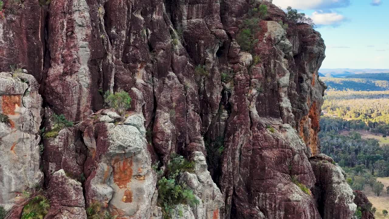 Drone pans over volcanic sandstone cliffs, revealing bushland and distant horizon in sunset light