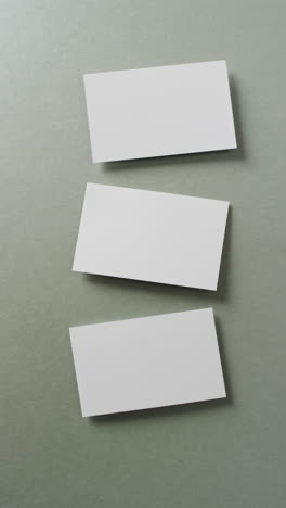 vertical video of blank white business cards on green background, copy space, slow motion