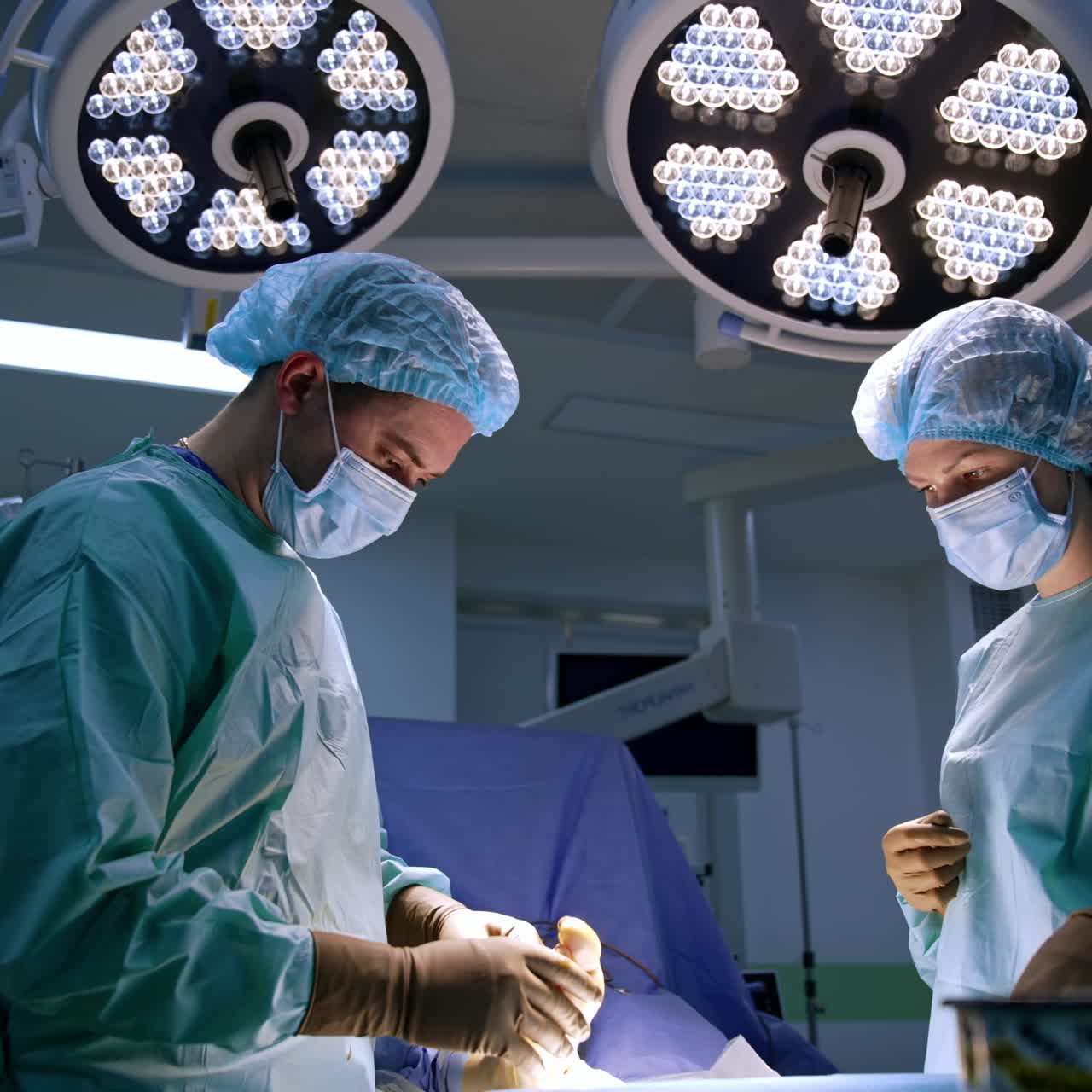 Mid aged male surgeon holding a patient's foot sewing the operated area. Female nurse stands watching beside