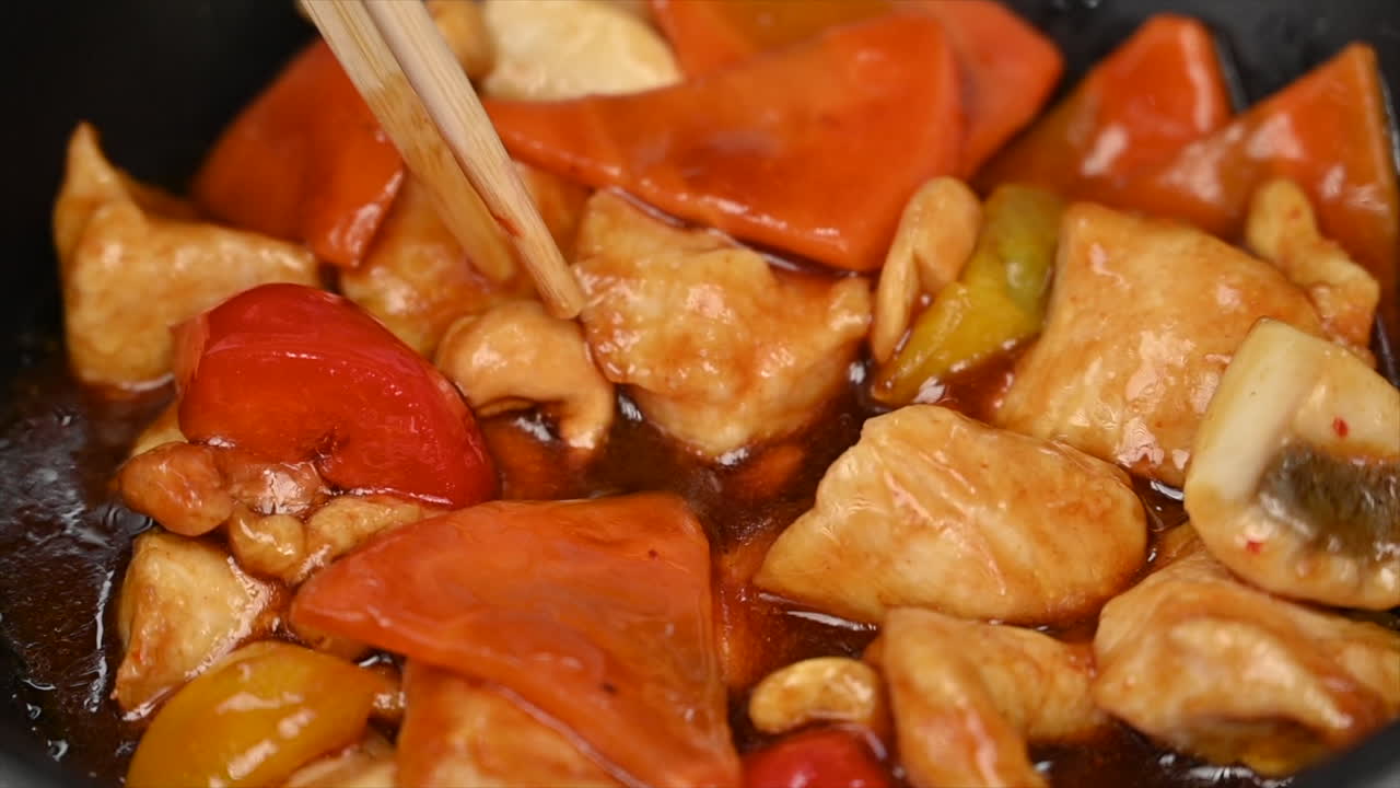 Woman eating chicken with vegetables and sweet sauce in a black pan at a chinese restaurant