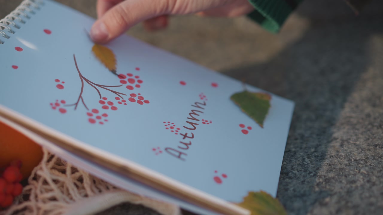 Persona che posa una foglia autunnale su un taccuino decorativo a tema stagionale.
