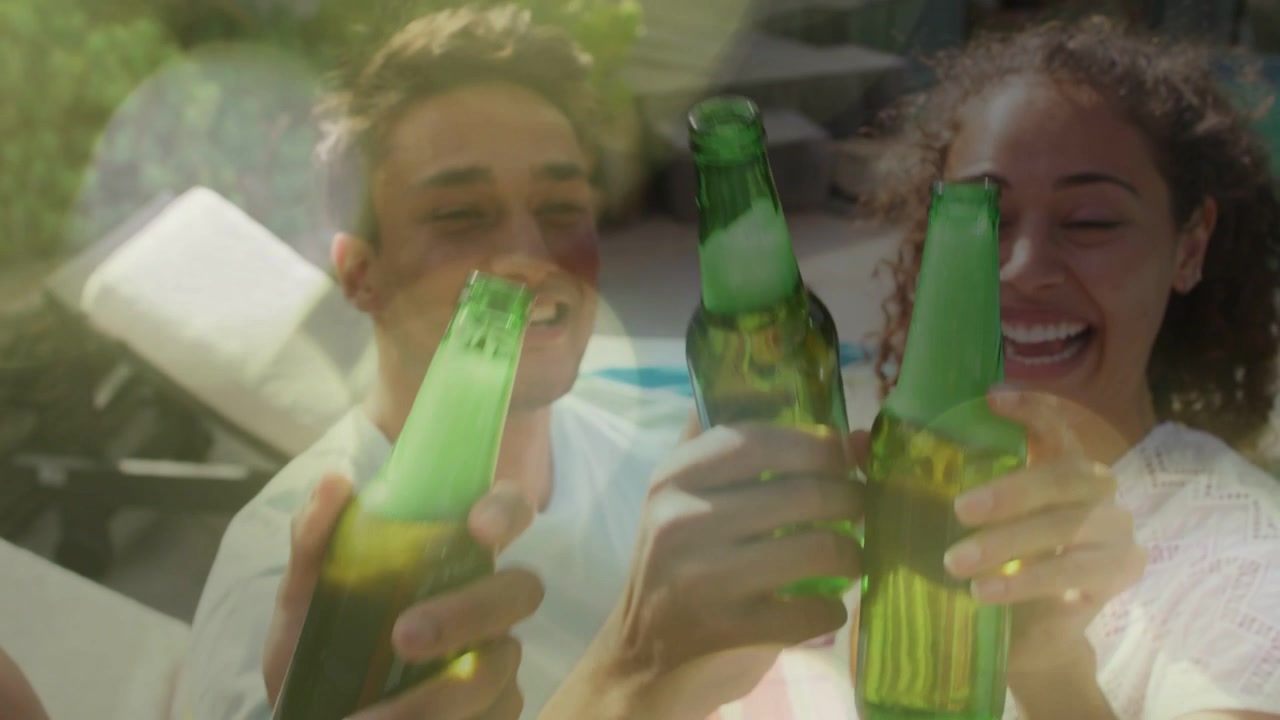 Scena lifestyle'owa z przyjaciółmi podnoszącymi zielone butelki przy basenie, podczas gdy nakładka bokeh się rozjaśnia, wznosząc toast